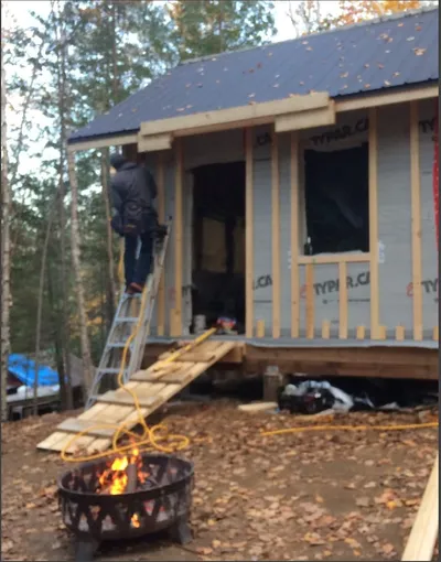 A worker on a ladder works on a wall, with a fire pit visible below.