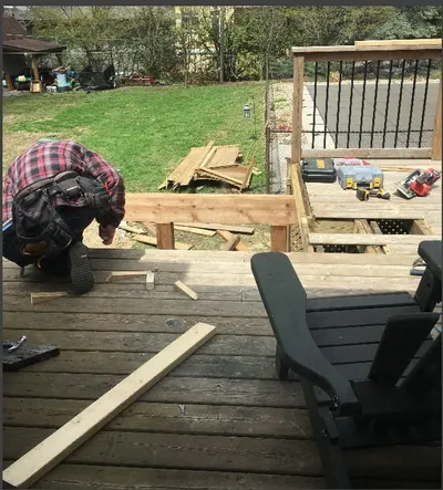 A worker kneels while fastening deck boards, surrounded by tools.