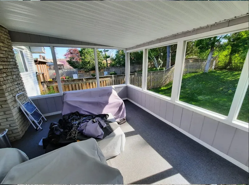 An existing three-season porch with furniture covered by tarps, before renovation work begins.
