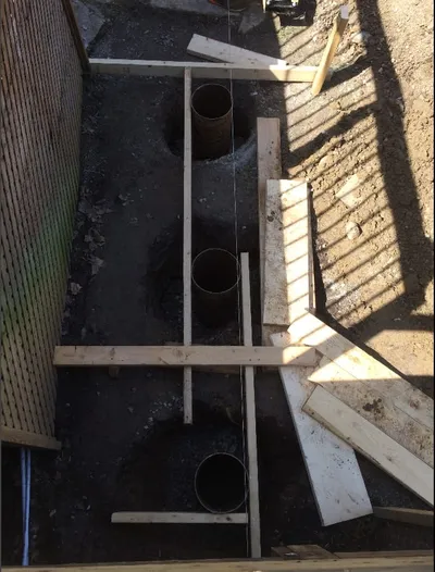 New footing forms are set in a trench for a deck foundation.