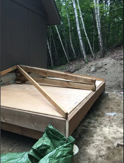 A framed deck platform with a plywood subfloor is built onto the side of a building.